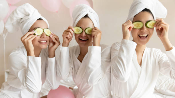 happy young women make cucumber mask relaxing together with balloons - facial mask spa treatment cucumber human face imagens e fotografias de stock