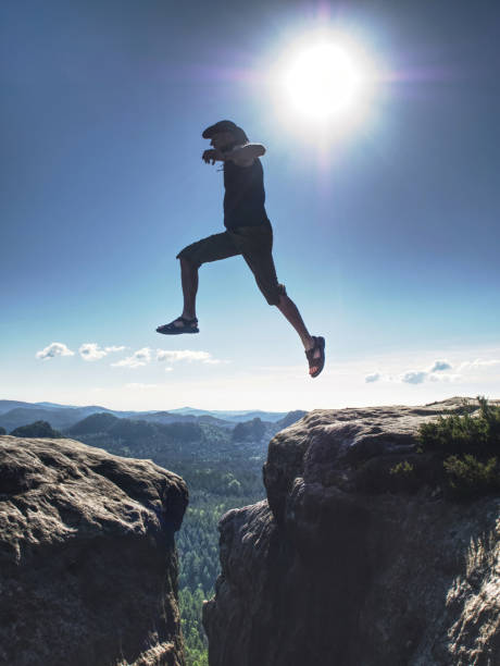 istock Jumping against Sun. Jumps over cliff. Man on trail through rocks/J 1190349910