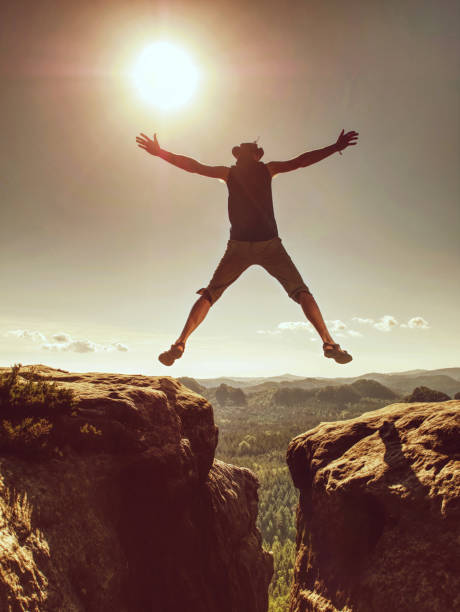 istock Jumping against Sun. Jumps over cliff. Man on trail through rocks/J 1190350490