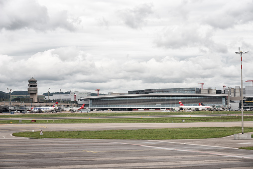 Zurich, Switzerland - August 10, 2019:  View to the main building of airport Zurich in Switzerland on a cloudy day. The airport runaway on the foreground and some Swiss and Edelweiss airplanes in the background are waiting for boarding.
