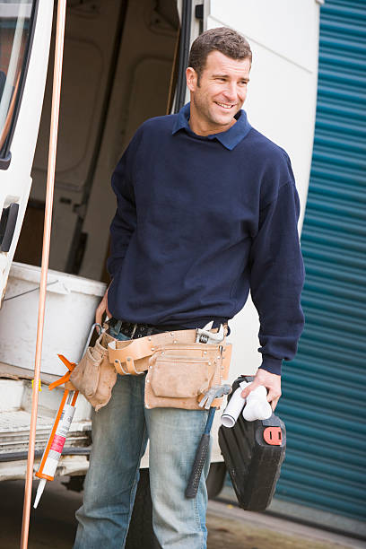 istock Smiling plumber with belt of tools standing with van 119035345