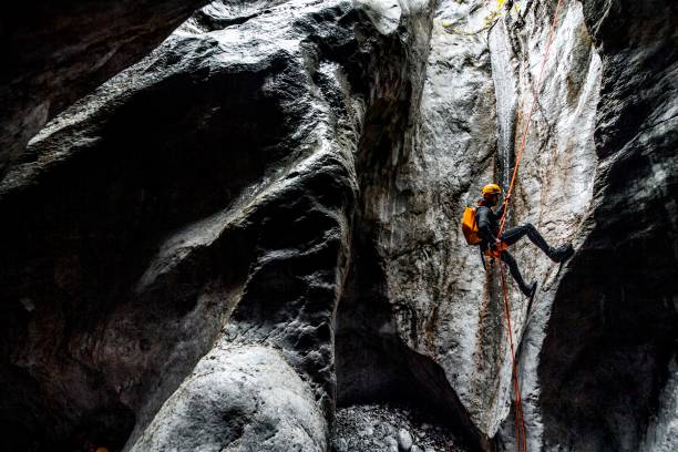 un maschio canyoning che fa un calale di corda lungo la corda statica in una grotta di pietra scura - arrampicata su roccia foto e immagini stock