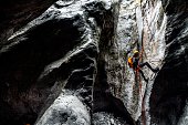 A canyoneering male making an abseil down the static rope into a dark stone cave