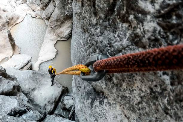 istock A carabiner holding two static ropes together. There's a canyoneer on the cliff bottom pulling at the end of the lower one 1190356155