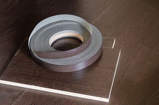 Edging tape lying on laminated chipboard sheets wenge color. Roll melamine edge for finishing of furniture.