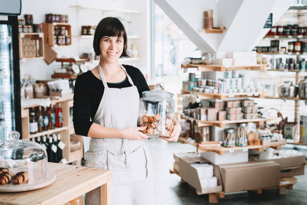 small local business owner. seller assistant with glass jar of pastries in interior of zero waste shop. - small business built structure retail imagens e fotografias de stock