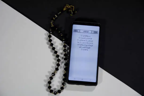 Top angle view of E Quran mobile app Quran in a mobile with a Tasbeeh Paternoster on black and white background