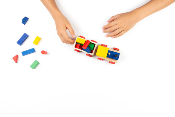 istock Kid hands playing with toy train and colorful wooden cube blocks on white table background. Top view 1190363509