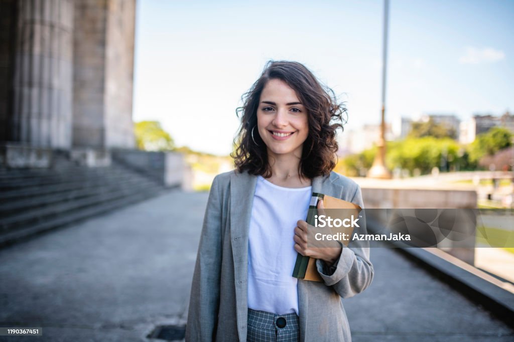 Law Student Standing at Entrance to University Building Close-up of relaxed female law student in casual attire standing with book at entrance to university in Buenos Aires. University Student Stock Photo