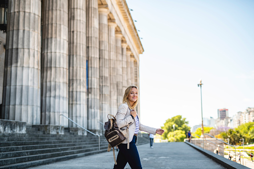 Side view of happy blonde law student with backpack leaving university building to enjoy spring day in Buenos Aires.