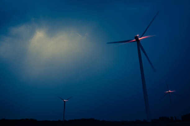 Wind turbines on a dramatic dark blue clouds in the sky. Storm ahead is coming. Red warning light on the windmill