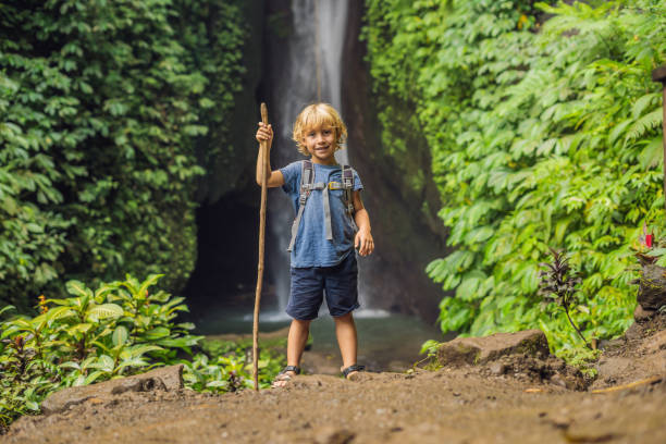 niño con un bastón de trekking en el fondo de la cascada leke leke en la isla de bali indonesia. viajar con niños concepto - mountain stream fotografías e imágenes de stock