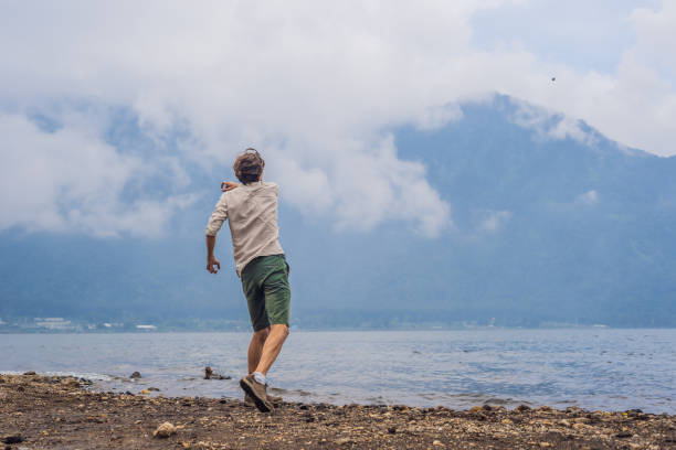 ブラタン湖と雲に覆われた山々の男性観光客 - throwing people stone tossing ストックフォトと画像