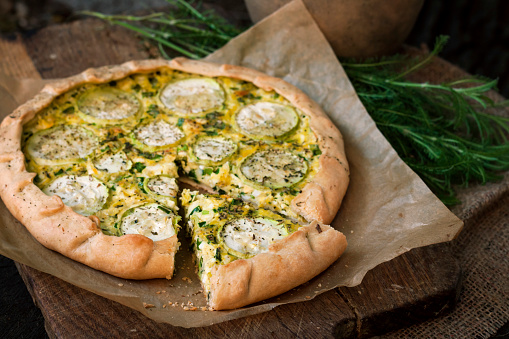 Homemade courgette and goat cheese pie on a dark rustic wooden board background