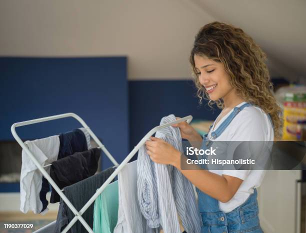 Young Woman Hanging The Laundry On Drying Rack Smiling At Home Stock Photo - Download Image Now