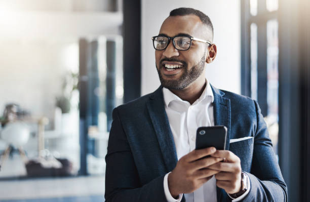 The ease that mobile technology brings Shot of a young businessman using a cellphone in an office business man looking away stock pictures, royalty-free photos & images