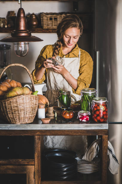 junge blonde frau in leinen schürze kochen hausgemachte gemüsekonserven - rustic domestic kitchen canning vegetable stock-fotos und bilder