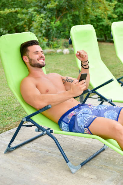 istock Young man on a sun lounger by the pool is using a cellphone 1190383791