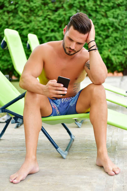 istock Young man on a sun lounger by the pool is using a cellphone 1190384986