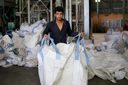 A male adult is holding bag getting ready to fill in one tonne processed rice at paddy factory.