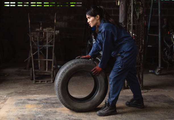 Diverse Asian car auto mechanic pushing worn tyre out of repair shop stock photo