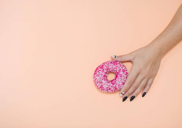 istock Appetizing donuts with icing on a colored background with female hands with a beautiful manicure. 1190394849