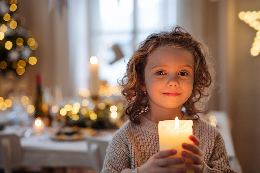 Chica pequeña alegre de pie en el interior en Navidad, sosteniendo la vela. photo