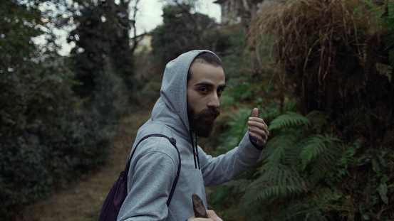 Side view of a young handsome bearded man with backpack walking in an old path in woods