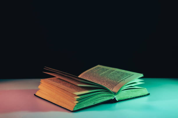 istock Beautiful open old book in the color light on a table and night background. 1190405260