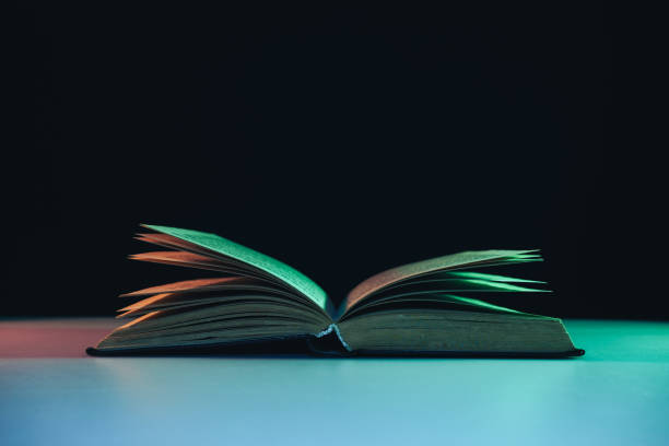 istock Beautiful open old book in the color light on a table and night background. 1190405483