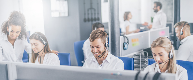 Call center worker accompanied by his team. Smiling customer support operator at work. Young employee working with a headset.