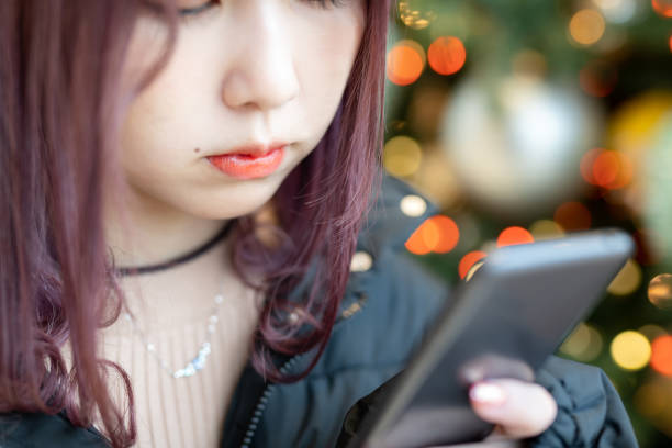 nastoletnia dziewczyna ze smartfonem stojącym przed choinką - christmas women human lips female zdjęcia i obrazy z banku zdjęć