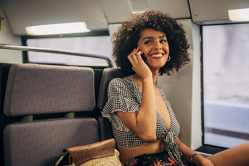 One woman, beautiful curly haired young lady sitting in train, talking on mobile phone.