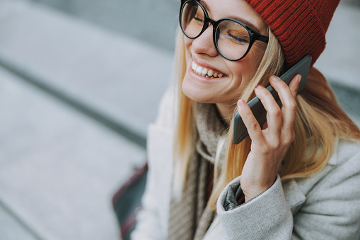 Laughing woman with rejoiced face smiling wide and using mobile phone