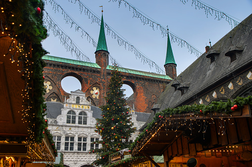 Christmas market with stalls, decorated with fir branches and light chains in front of the historical town hall in the hanseatic old town of Luebeck, Germany