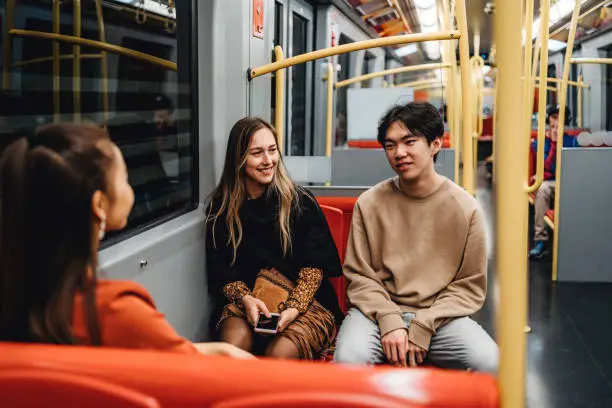 Chinese and Caucasian teenagers taking a ride in a subway train together.