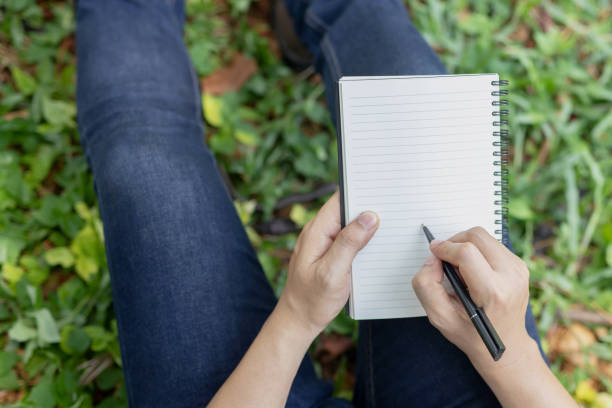 istock close up hand young man are sitting using pen writing Record Lecture notepad into the book in the park. Top view. 1190424319