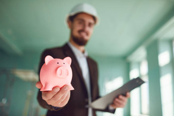 The concept of savings in construction. The builder foreman is holding a piggy bank in his hand.