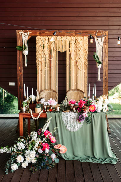 istock Elegant newlyweds table in boho style with a green tablecloth and flowers, wicker macrame arch in the background 1190430207