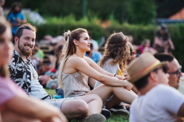 gruppe junger freunde, die beim sommerfest auf dem boden sitzen. - freiluftkonzert stock-fotos und bilder