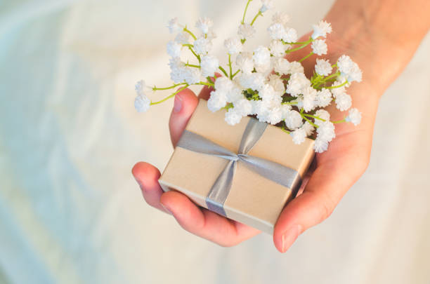 istock Female hand holds a small gift box and white flowers 1190439404