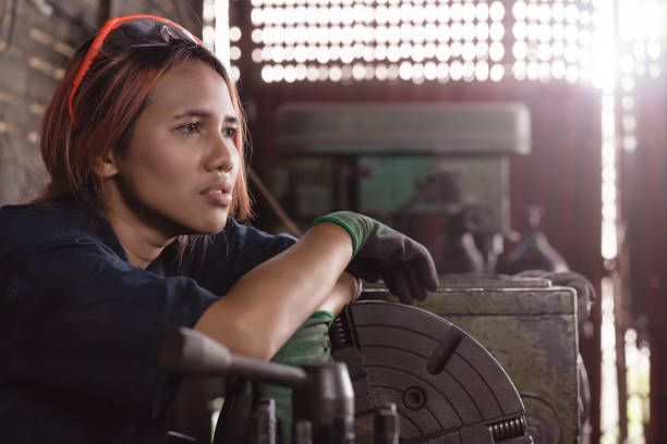 Exhausted and fatigued diverse Asian female engineer taking a break on industrial machinery in factory stock photo