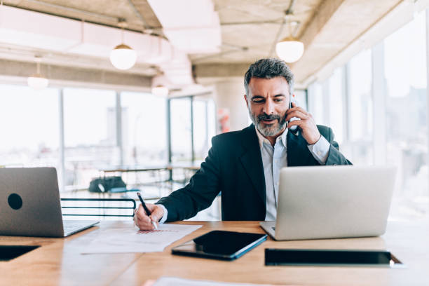 Businessman at the office talking on cell phone Businessman at the office talking on cell phone financial occupation stock pictures, royalty-free photos & images