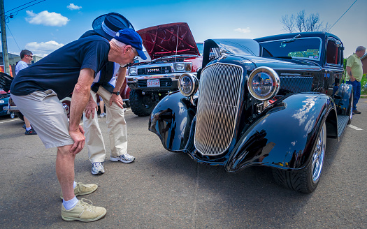 Moncton, New Brunswick, Canada - July 10, 2015 : 1933 Plymouth 5 window coupe parked in downtown area of Moncton during Atlantic Nationals Automotive Extravaganza. An older man gives the hot rod a close look.