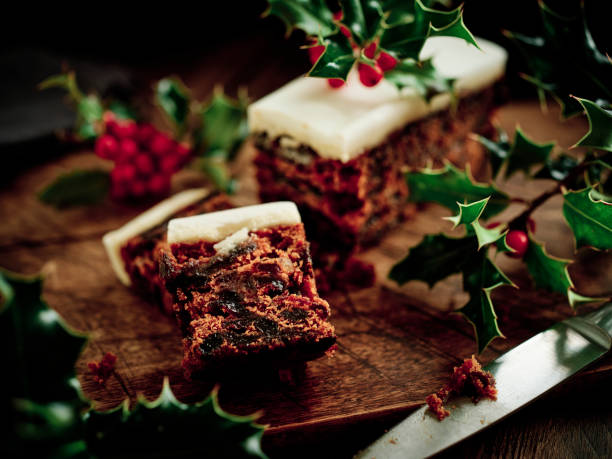 bolo de natal em uma superfície de madeira rústica escura cercada por holly recém-escolhido. - bolo de natal - fotografias e filmes do acervo