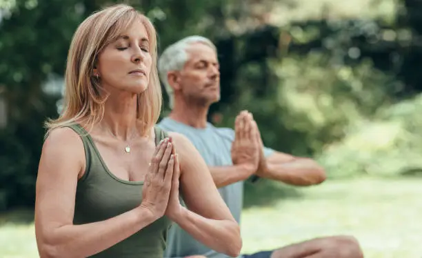 Mature couple doing the cross legged seated pose while sitting with their eyes closed outside during yoga practice