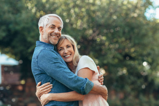 sonriendo pareja madura affectionatley abrazándose entre sí fuera - mature adult couple caucasian outdoors fotografías e imágenes de stock