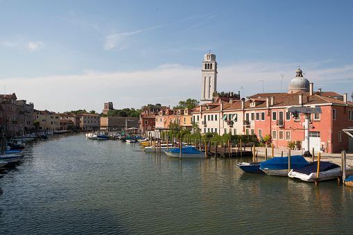 Murano, Italy, September 14, 2019: bridge across water canal, boats and motor boats, colorful traditional buildings, Venetian Lagoon, Veneto Region. San Michele in Isola Catholic church background