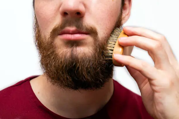 closeup of handsome man brushing his beard on white background isolated beauty