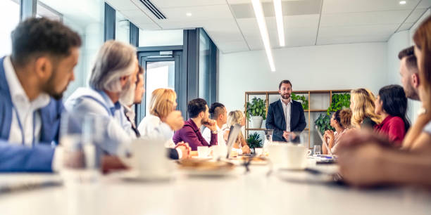 caucasian businessman giving a speech to people sitting at a conference table - business business person ceo coffee imagens e fotografias de stock